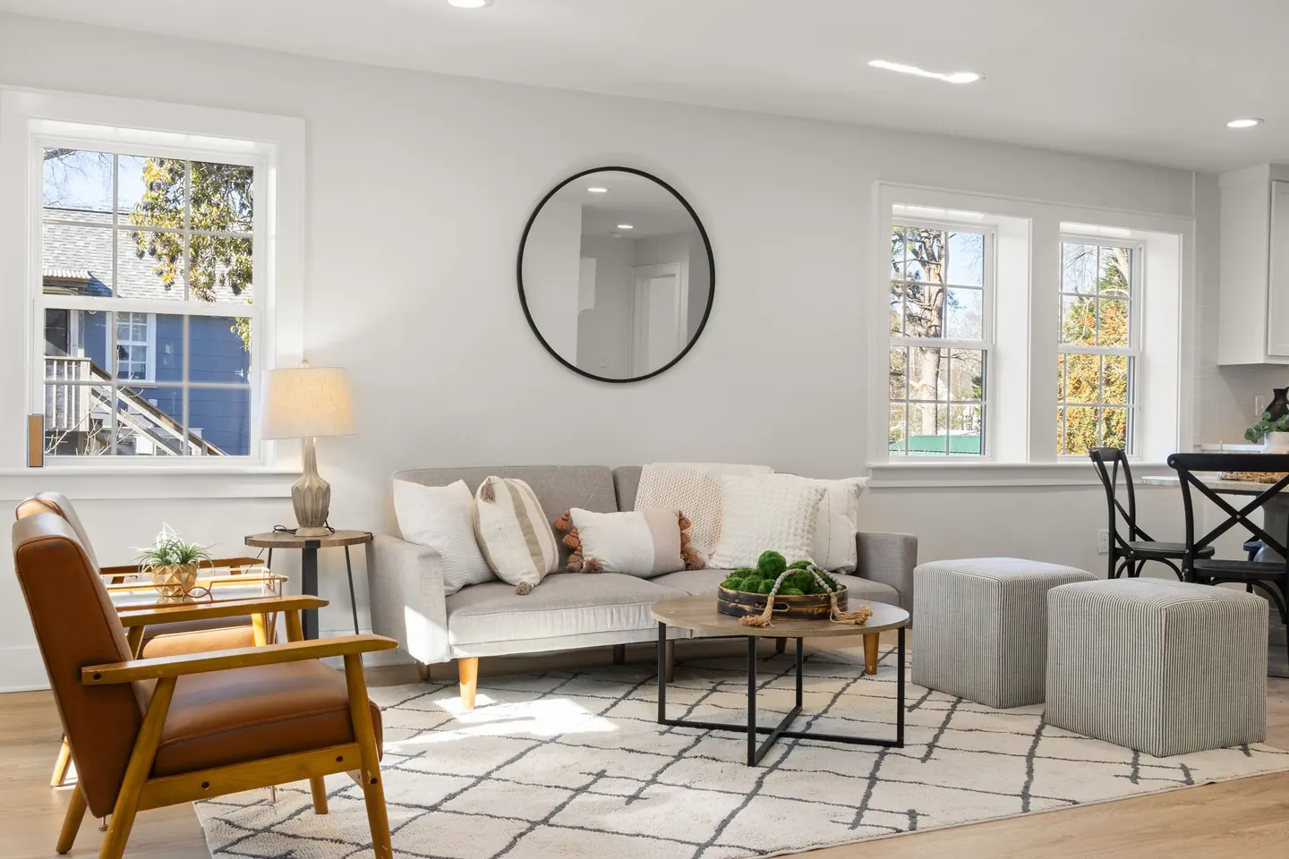 Canapé gris clair avec des coussins écrus, un tapis et une table basse dans un salon éclairé par les fenêtres